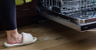 A person loading a dishwasher with Coretec vinyl flooring visible