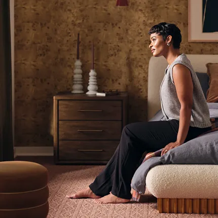 Warm Brown Synthetic Carpet in Bedroom Scene Cozy bedroom with synthetic carpet in a warm brown tone, featuring a woman sitting on a bed