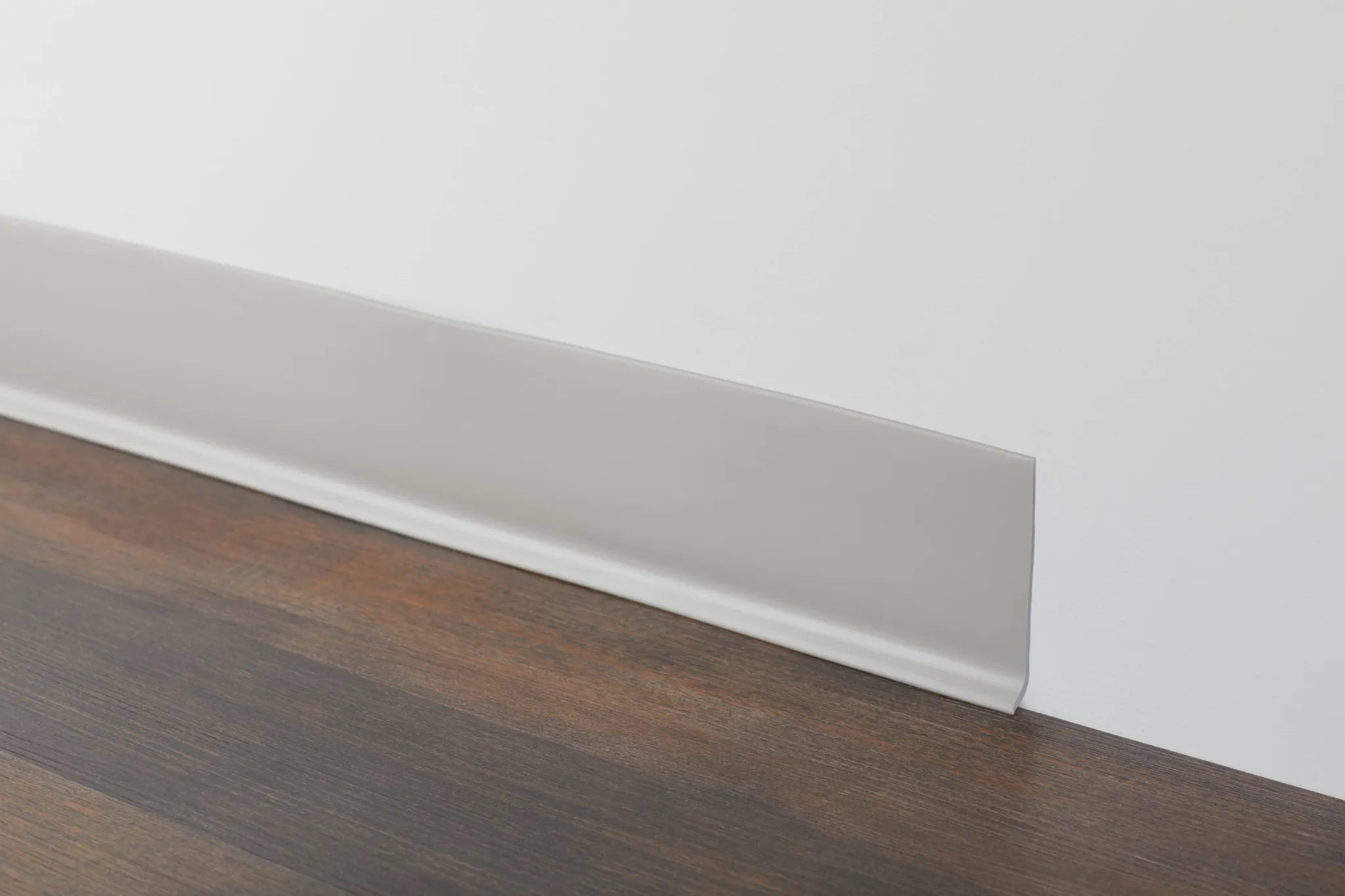 Dark wood flooring with white baseboard in a room setting