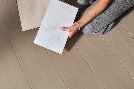 Coretec Residential WPC Vinyl Flooring - 59.84x7.05 inch - Beige and White Marble Patterns Woman in gray outfit holding two vinyl tile samples in beige and white marble patterns on wood look vinyl flooring