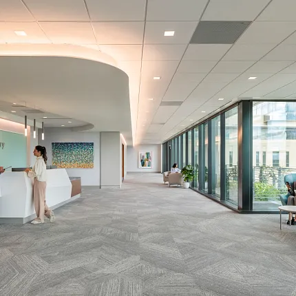 Healthcare Facility Lobby with Commercial Carpet Tile Flooring Modern healthcare facility lobby with commercial carpet tile flooring, featuring a doctor and a woman at the reception desk, large windows, and seating area.