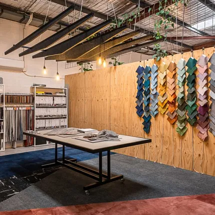 Colorful Carpet Swatches Display in Modern Showroom Modern showroom with a variety of colorful carpet swatches displayed on a wooden wall, featuring a mix of blue, green, orange, pink, and gray tones, with industrial lighting and shelving in the background
