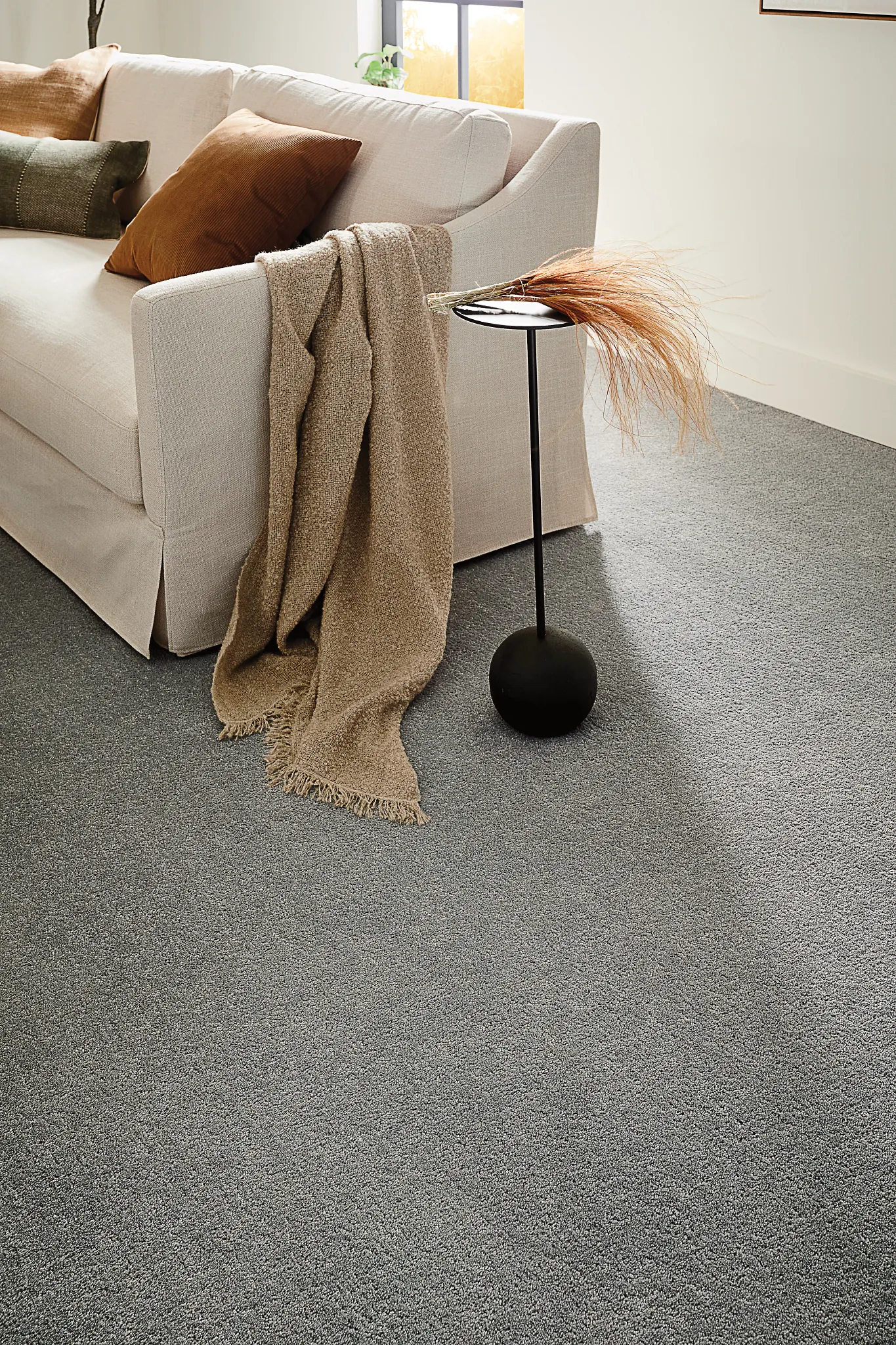 Cozy living room with a light beige sofa, earth-toned pillows, and a soft gray carpet flooring