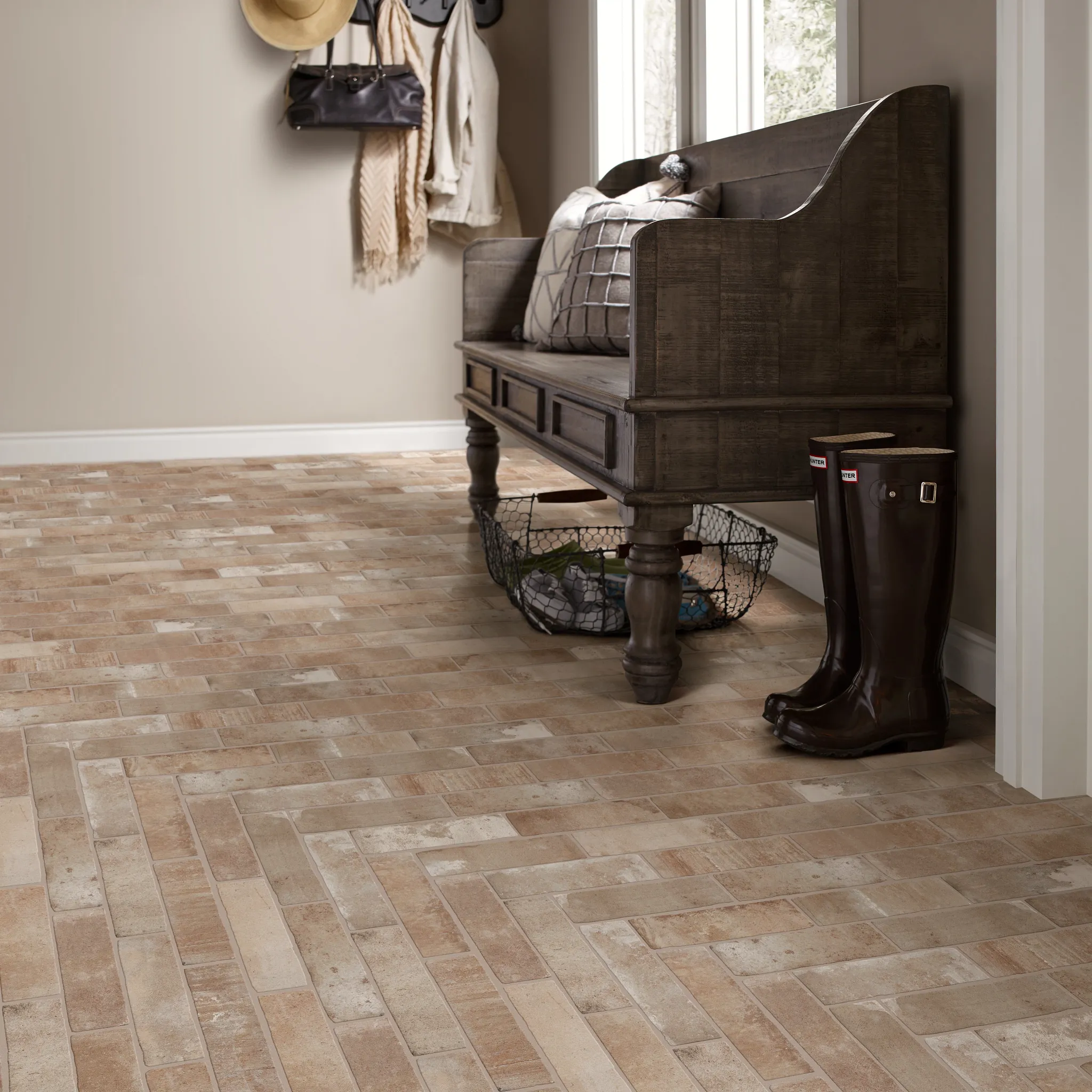 Rustic entryway with herringbone pattern flooring in shades of beige and brown, featuring a wooden bench and rain boots