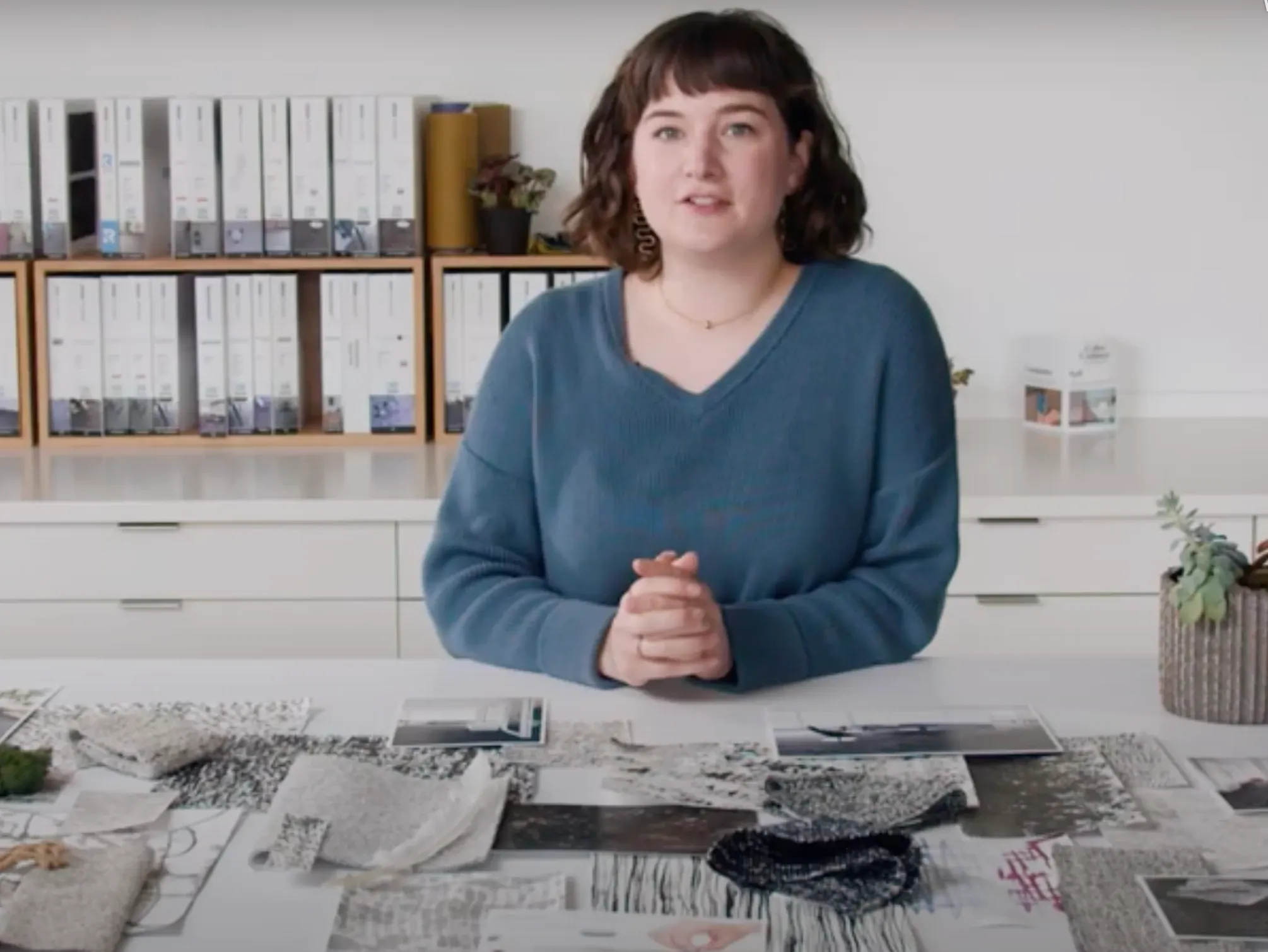 Woman in blue sweater reviewing various flooring swatches on a table in an office setting