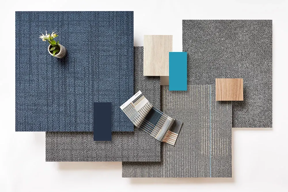 Swatch of commercial carpet tiles in various colors including blue, grey, and beige with a small plant on top