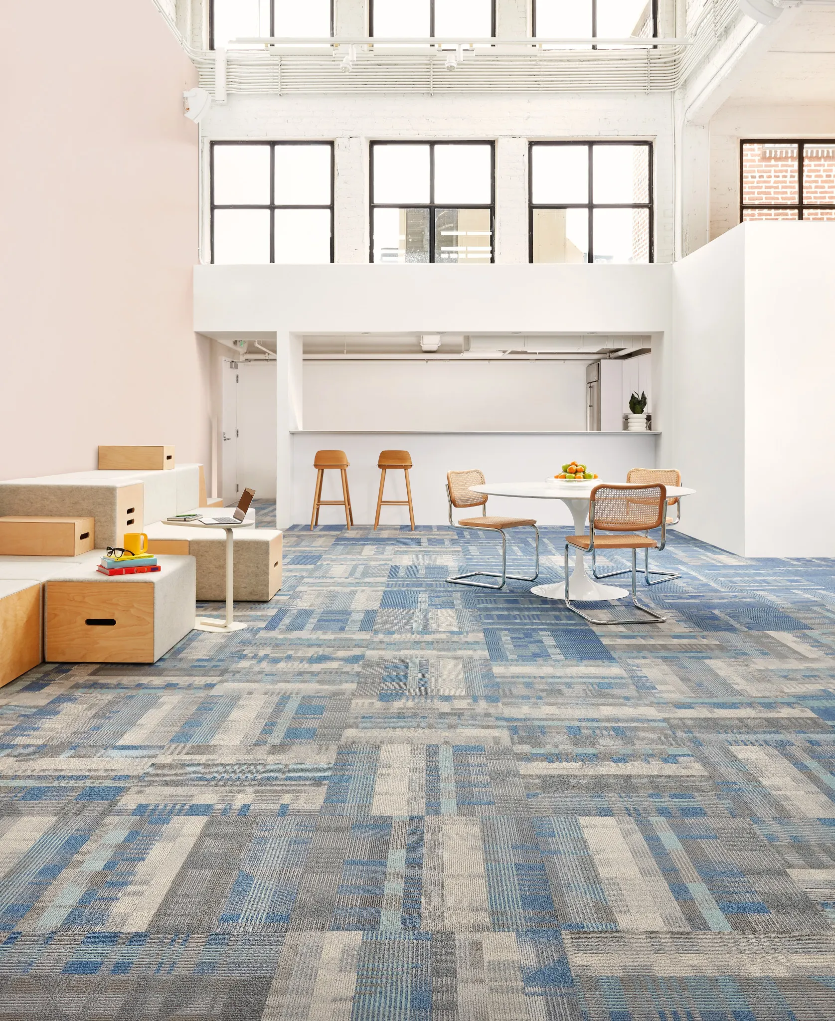 Instalación educativa contemporánea con alfombra modular comercial en tonos azul y gris, un interior amplio y luminoso, abundante luz natural y mobiliario contemporáneo.