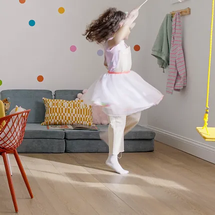 Wood Look Luxury Vinyl Plank Flooring in Playroom - Durable and Stylish Flooring Solution Modern playroom with a young girl dancing on wood look luxury vinyl plank flooring, featuring colorful chairs and wall decor.