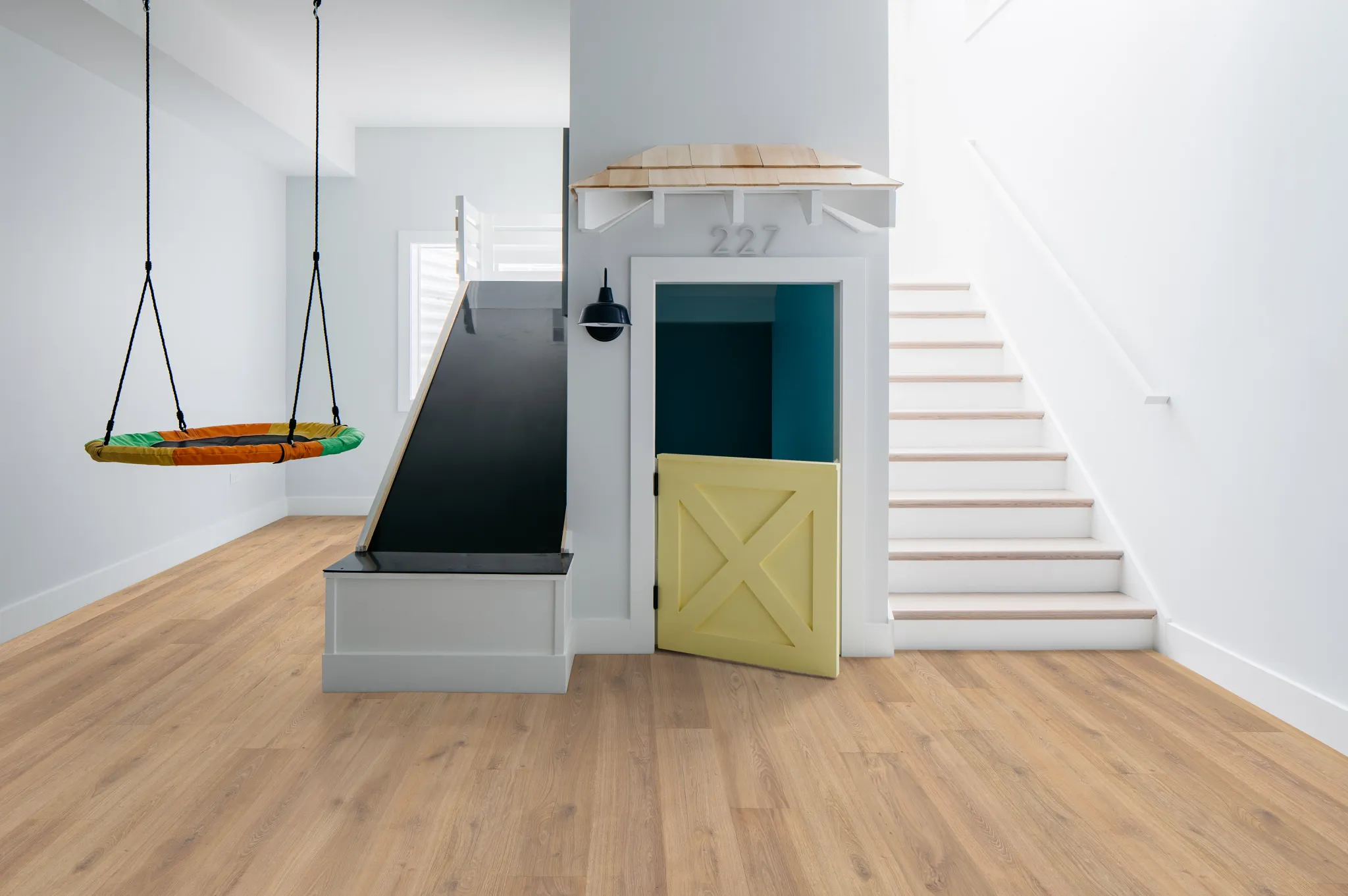 Modern playroom with light wood flooring, featuring a slide, swing, and small door