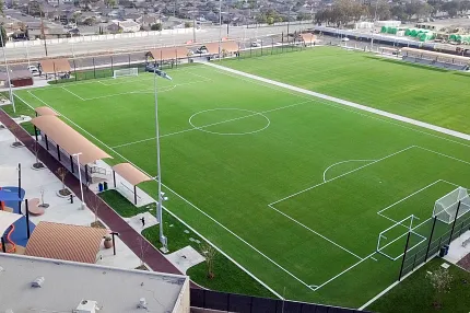 Artificial Turf Soccer Field with Playground and Parking Area Aerial view of a large artificial turf soccer field with white boundary lines and goalposts