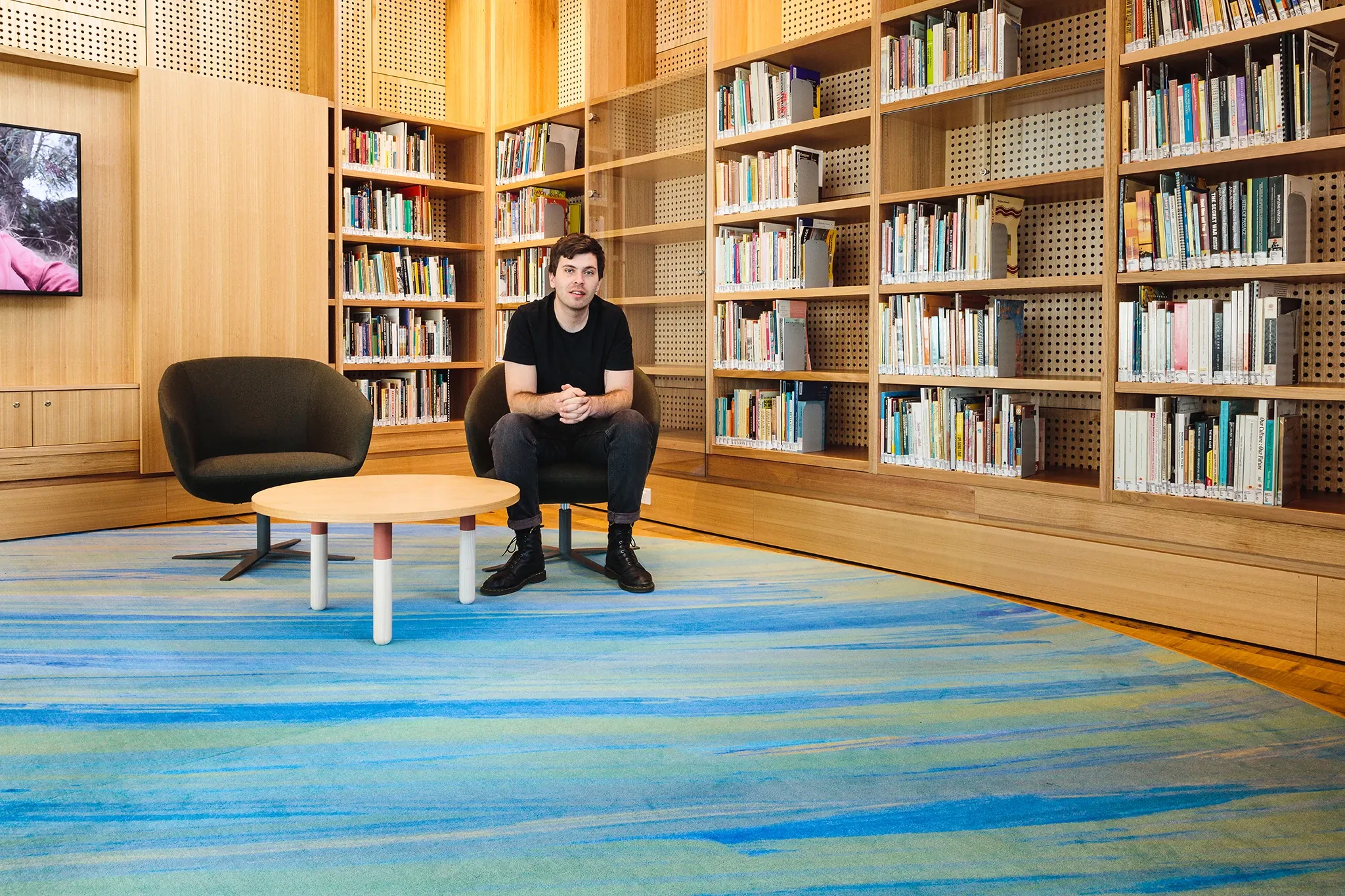 Modern library setting with blue and green commercial carpet tile, featuring bookshelves and seating area, Education Facility.