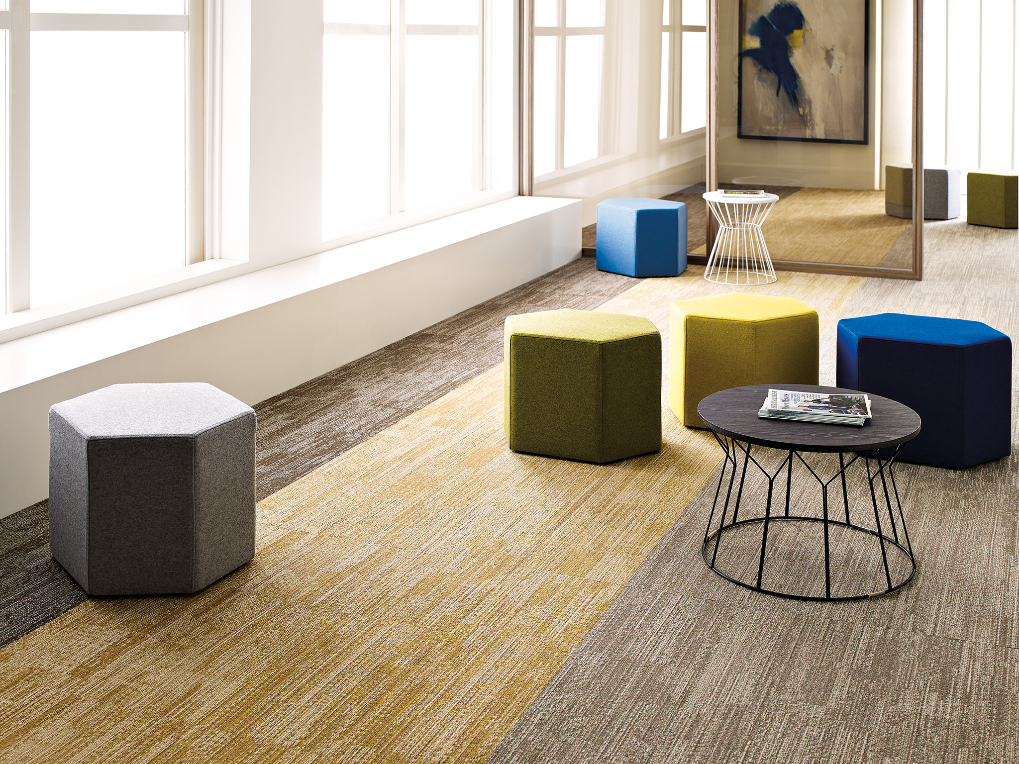 
  "office space with colorful ottomans and abstract art with commercial carpet floor in shades of gray and yellow"
)