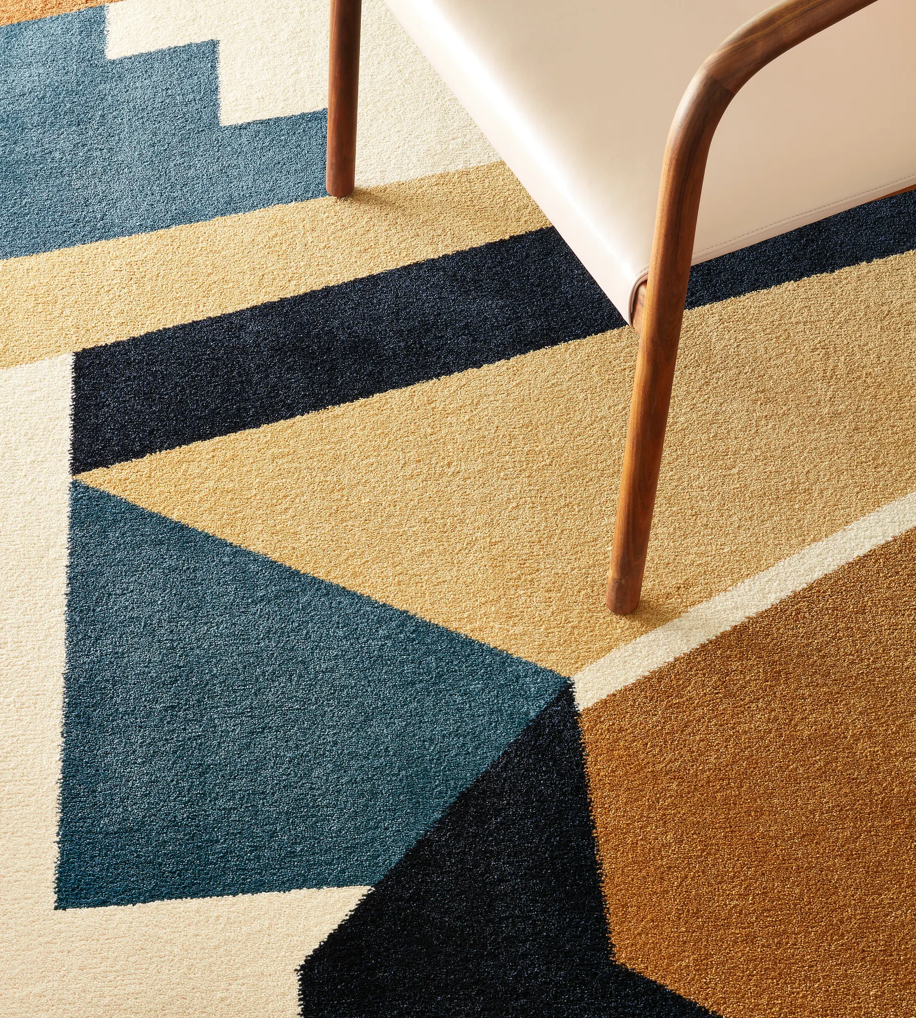 Geometric patterned commercial carpet in shades of blue, beige, and brown with a wooden chair leg