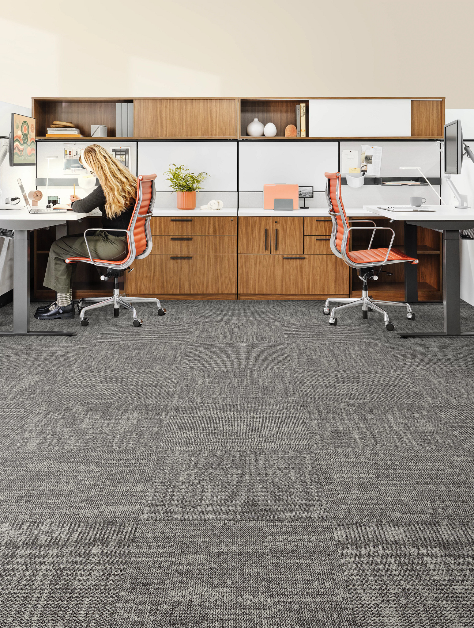 Modern workplace with gray commercial carpet tile flooring, featuring 24x24 inch tiles, and two desks with orange chairs and a woman working