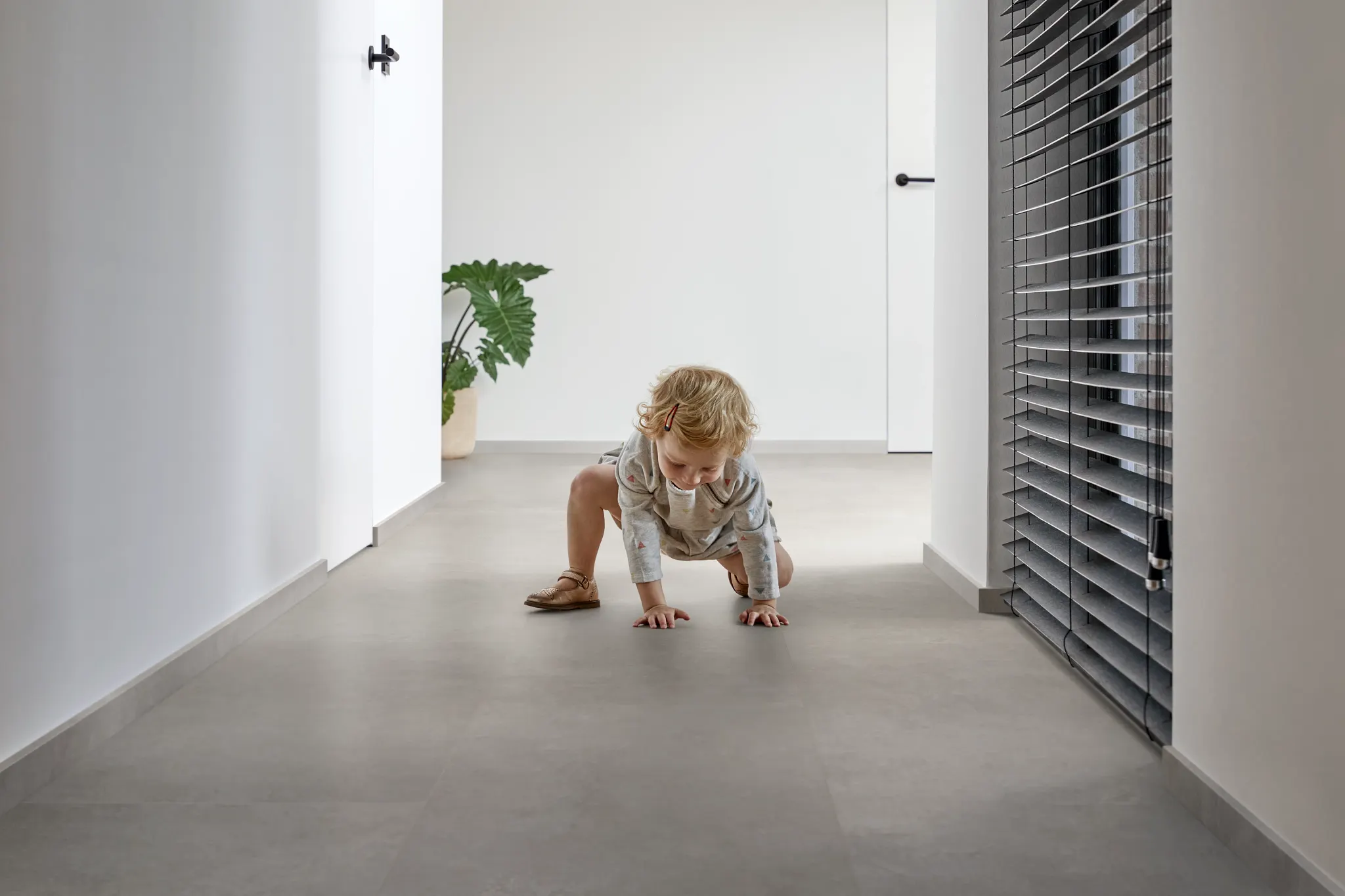 Modern hallway with luxury vinyl tile flooring in a light gray stone look, featuring a young child playing on the floor