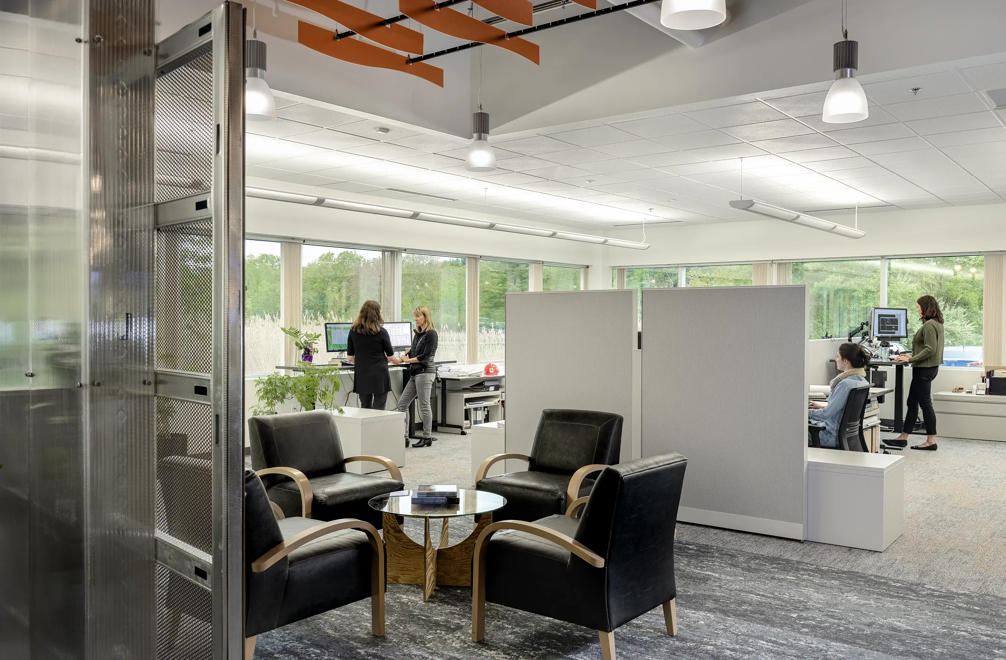 Modern workplace with open office layout featuring black armchairs and a round table on commercial carpet tile flooring