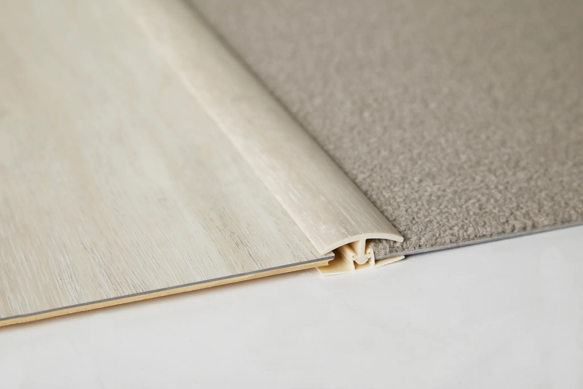 Transition strip connecting light wood-look flooring and beige carpet