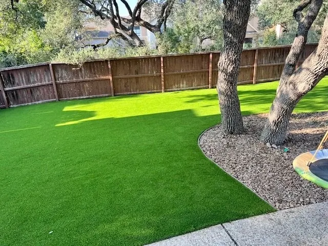 Artificial grass in a backyard setting with trees and fence