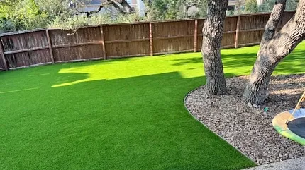 Lush green synthetic turf for outdoor spaces Artificial grass in a backyard setting with trees and fence