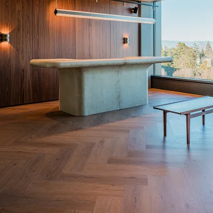 Modern reception desk with designer lighting, rich walnut storage room and rich wood herringbone floors