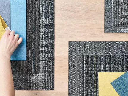 Commercial Carpet Tile Samples in Blue, Yellow, and Gray Hand arranging commercial carpet tile samples in blue, yellow, and gray on a wooden surface