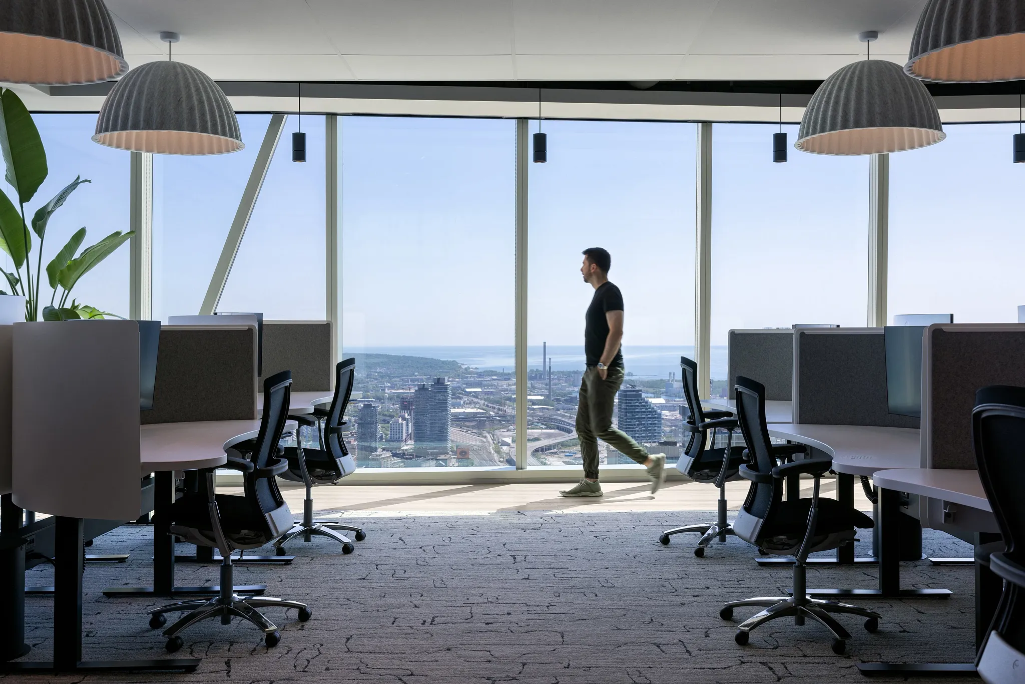 Modern office space with large windows and a man walking, featuring commercial carpet tile flooring in a workplace setting