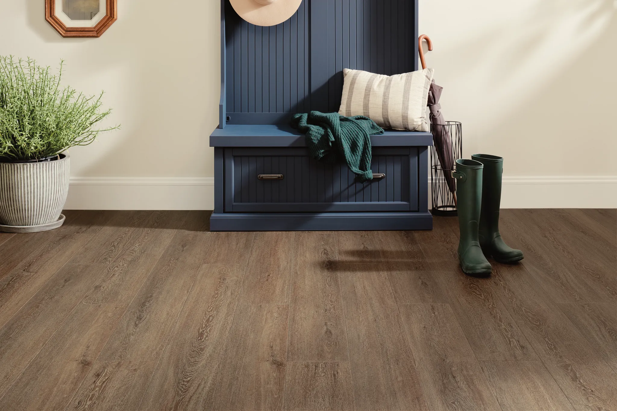 Residential entryway with wood look luxury vinyl plank flooring, featuring a blue bench, green boots, and a potted plant