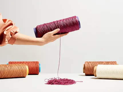 Colorful yarn spools for commercial carpet production Hand holding a spool of magenta yarn with other spools in orange, beige, and cream colors on a table