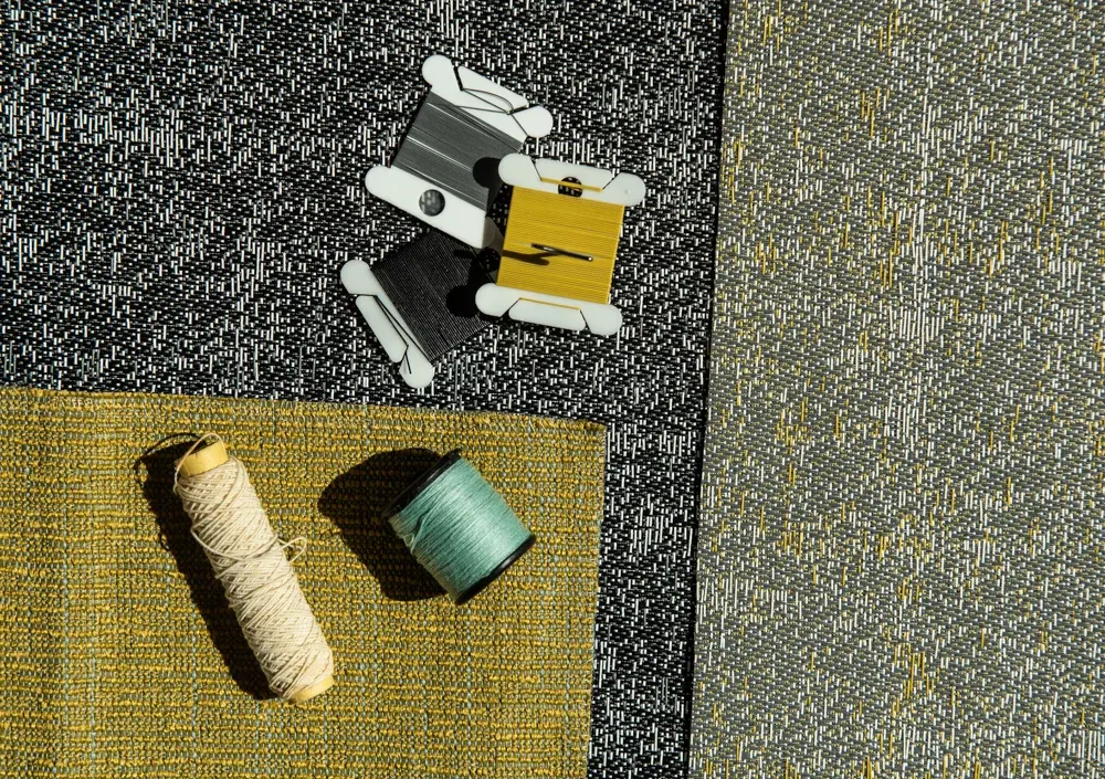 Muestra de alfombra modular comercial en negro, gris y amarillo, con carretes de hilo y muestras de color.