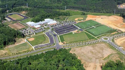 Sports complex with artificial turf fields aerial view Aerial view of a sports complex with multiple artificial turf fields surrounded by lush greenery