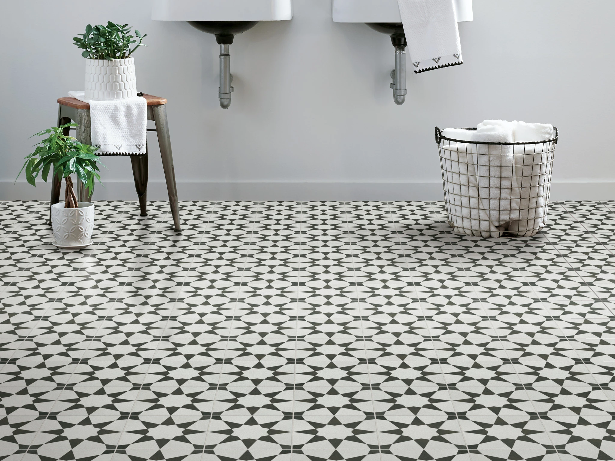 Geometric black and white patterned tile flooring in a modern bathroom with plants and towels