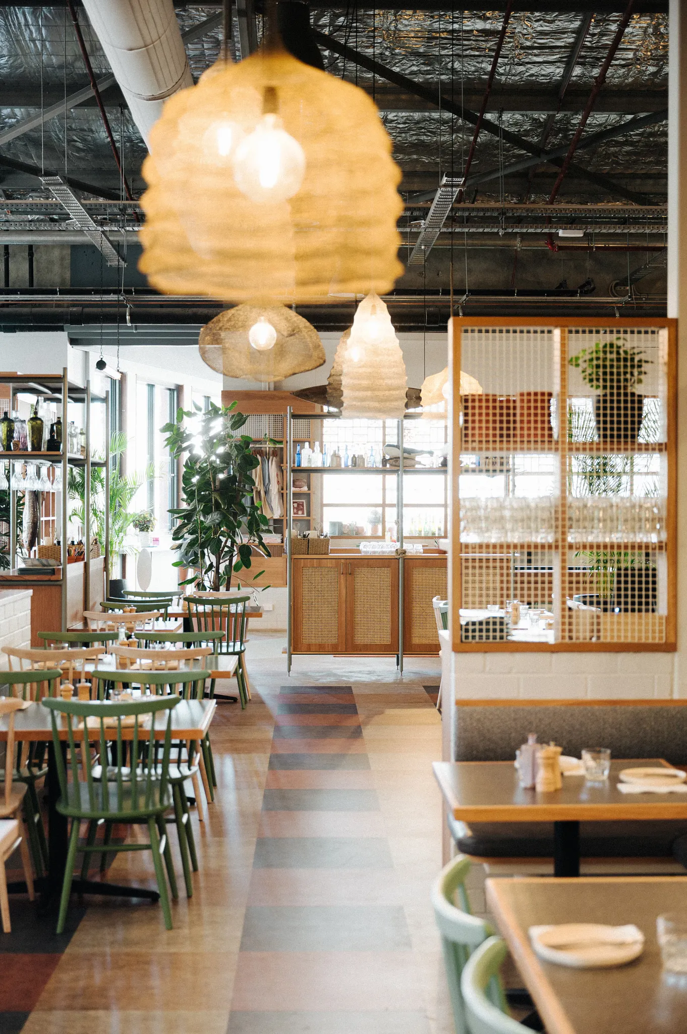 Modern restaurant interior with wooden tables and green chairs, featuring a mix of light and dark wood flooring