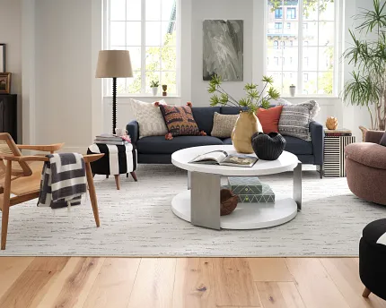 Contemporary living room with light wood flooring and stylish decor Modern living room with light wood flooring, featuring a navy sofa, colorful cushions, and a white round coffee table