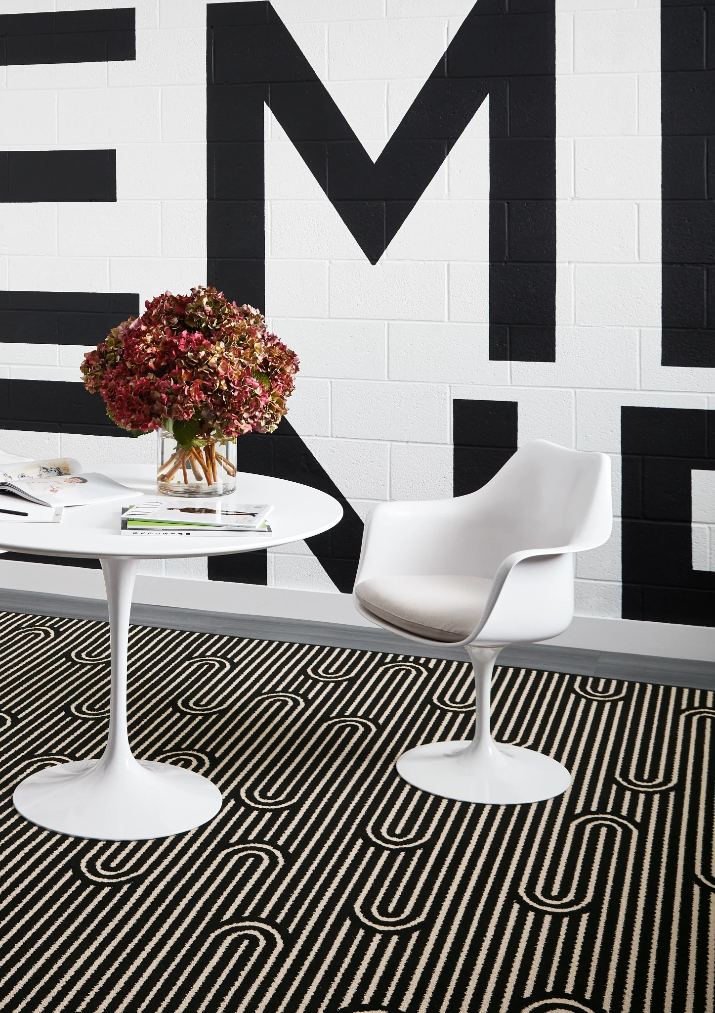Modern office space with black and white geometric broadloom carpet, white table and chair, and a large wall mural