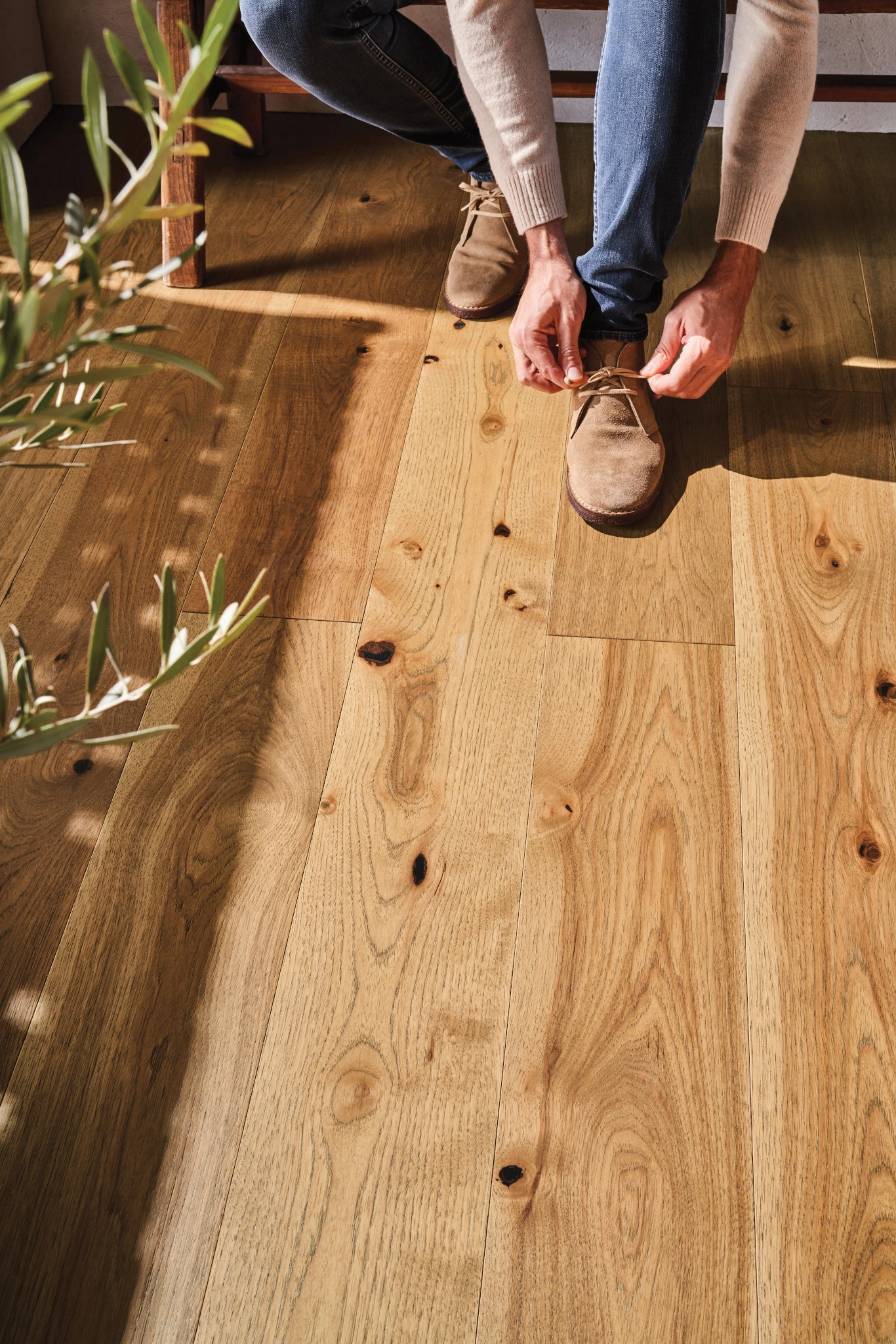 Man tying shoe on natural oak hardwood flooring with visible knots and grain