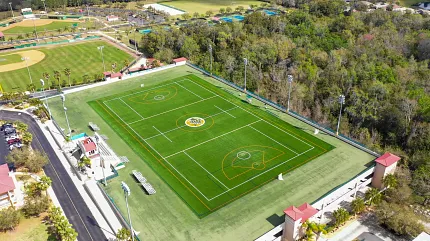 Sports complex with artificial turf field and surrounding landscape. Aerial view of a sports complex featuring an artificial turf field with marked lines for soccer and baseball