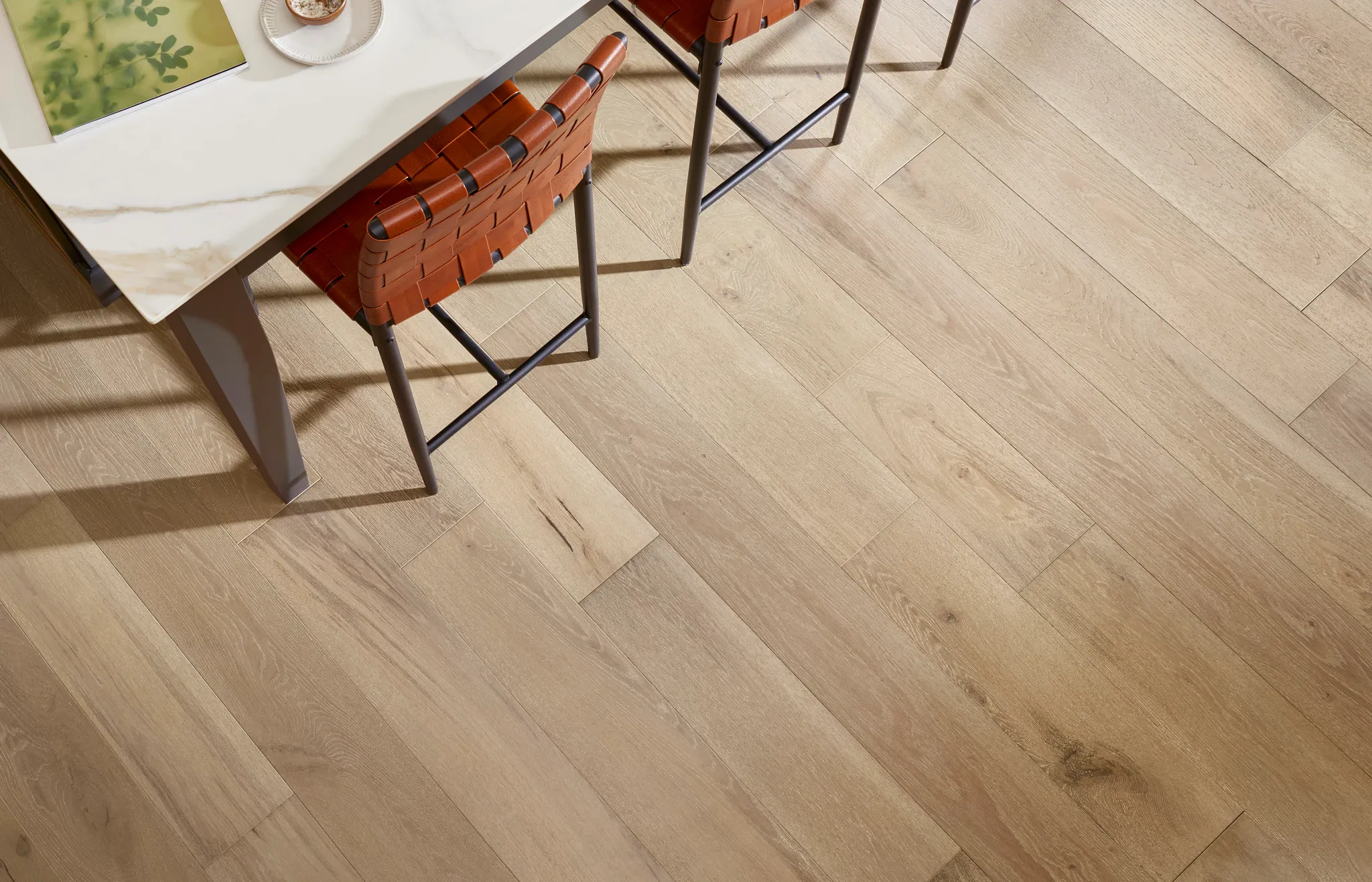 Elegant light brown hardwood flooring in a dining area with a modern table and leather chairs