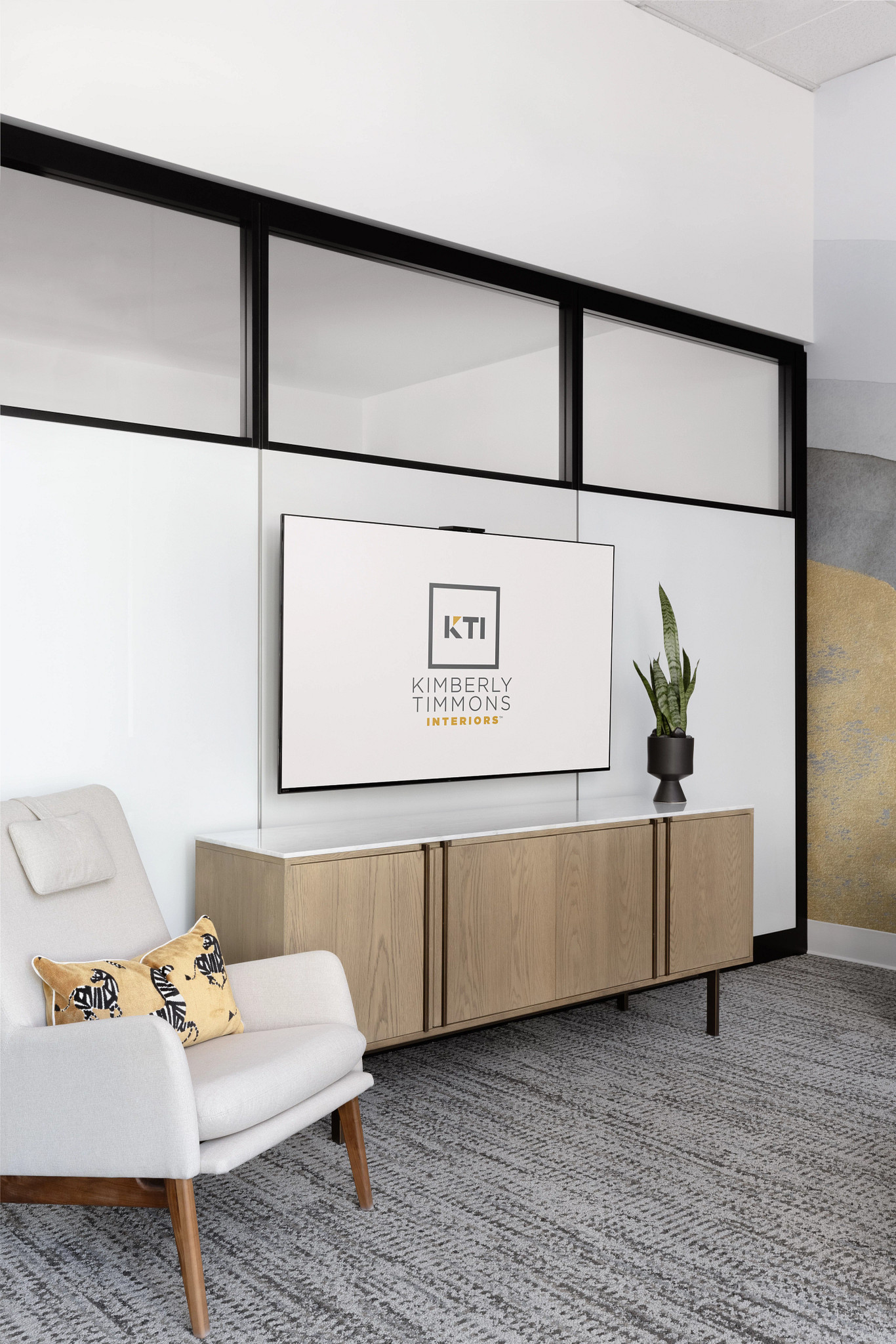 Modern workplace interior with light gray commercial carpet tile flooring, featuring a 9x36 inch pattern, a light wood cabinet, and a white armchair with a decorative pillow