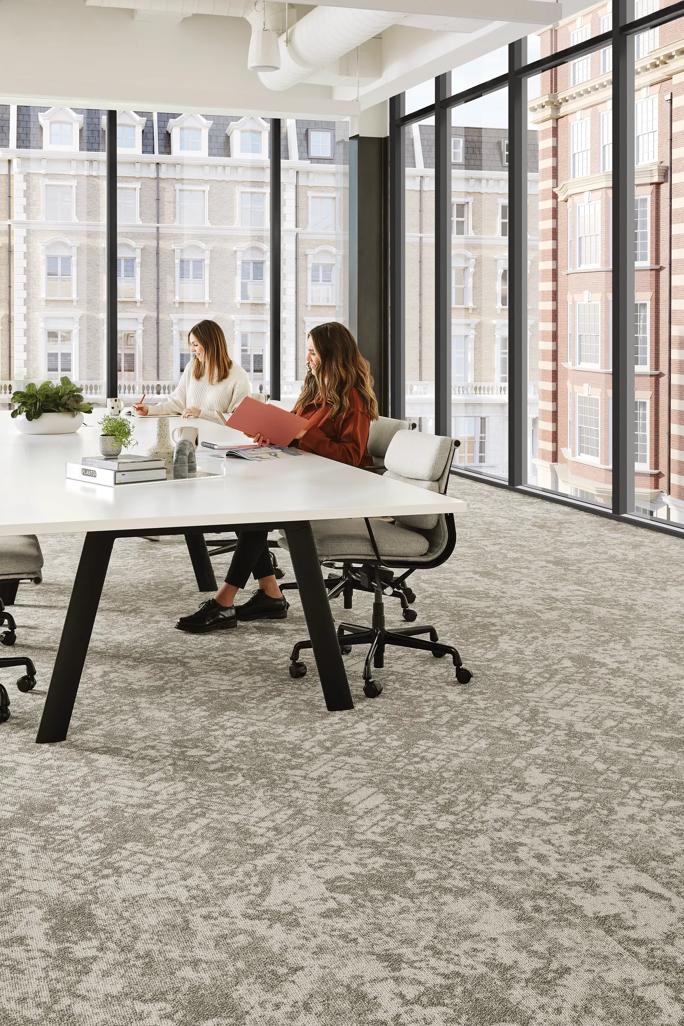 Modern workplace with gray commercial carpet tile flooring, featuring 24x24 inch tiles, and two desks with orange chairs and a woman working