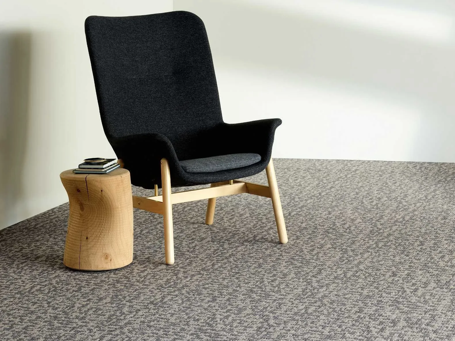 Modern lounge area with a black chair and wooden side table on patterned commercial carpet tile