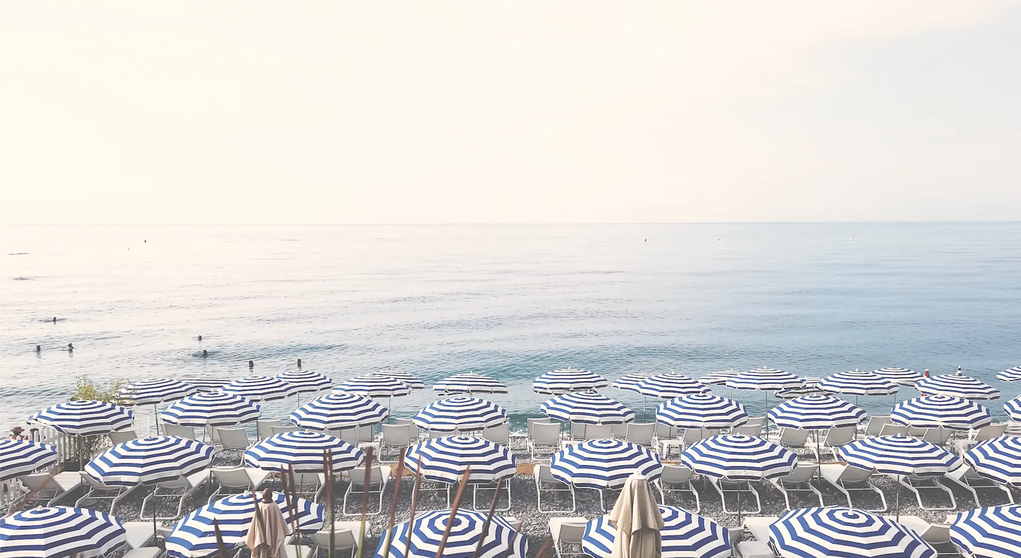 Beach scene with blue and white striped umbrellas and calm sea