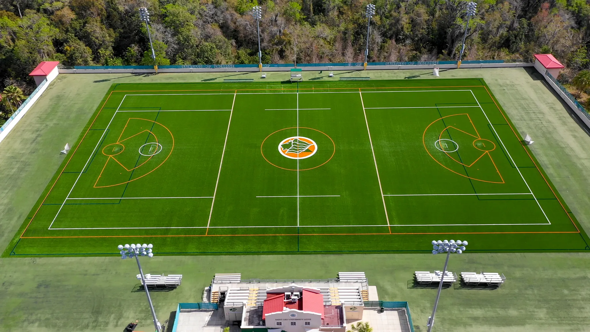 Aerial view of a green sports field with marked lines and surrounding trees