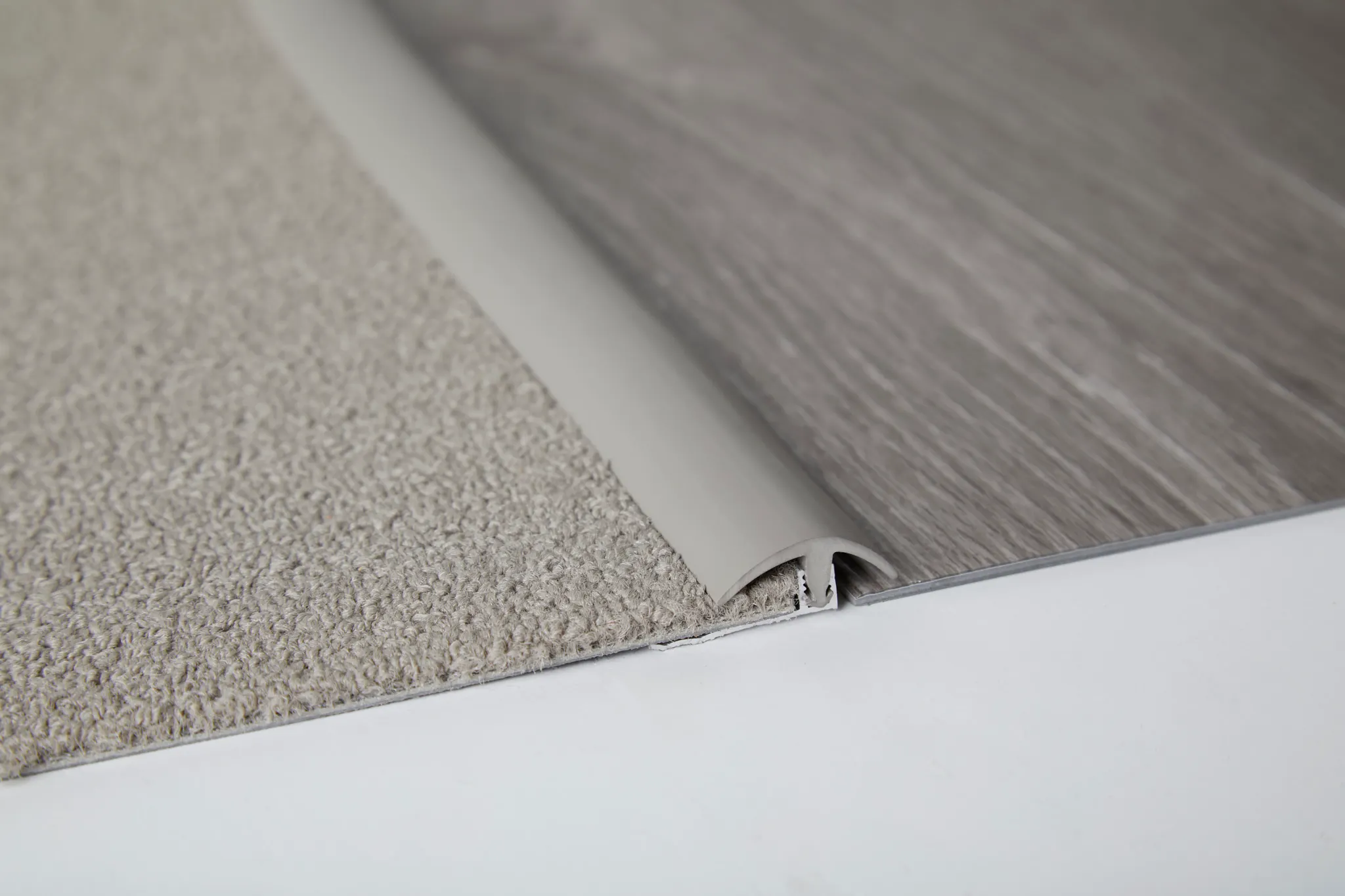 Close-up of flooring transition between beige carpet and gray wood-look flooring with a white trim