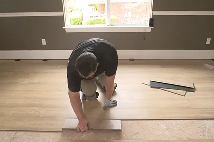Easy-to-maintain light oak luxury vinyl plank flooring installation for everyday comfort Man installing light oak luxury vinyl plank flooring in a living room