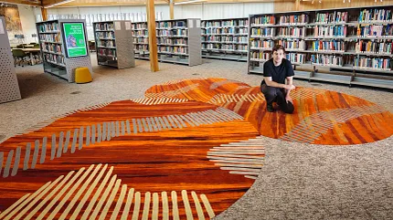 University of Tasmania Project Featuring Custom Flooring Design Collaboration | Shaw Contract Custom carpet flooring inspired by Indigenous artwork installed within the University of Tasmania library, shown alongside the collaborating artist.