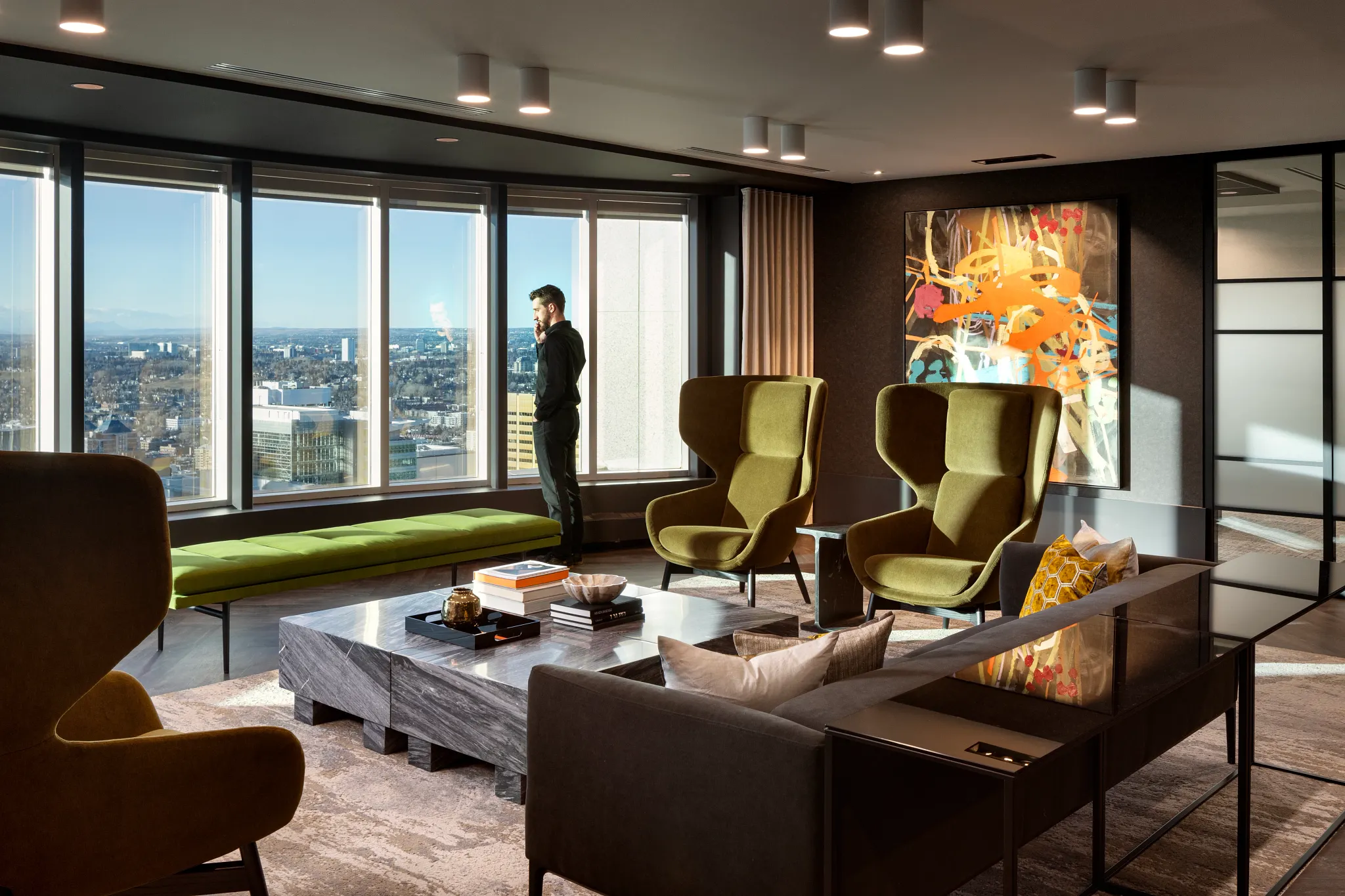Modern office lounge with large windows, green armchairs, and abstract art on the wall