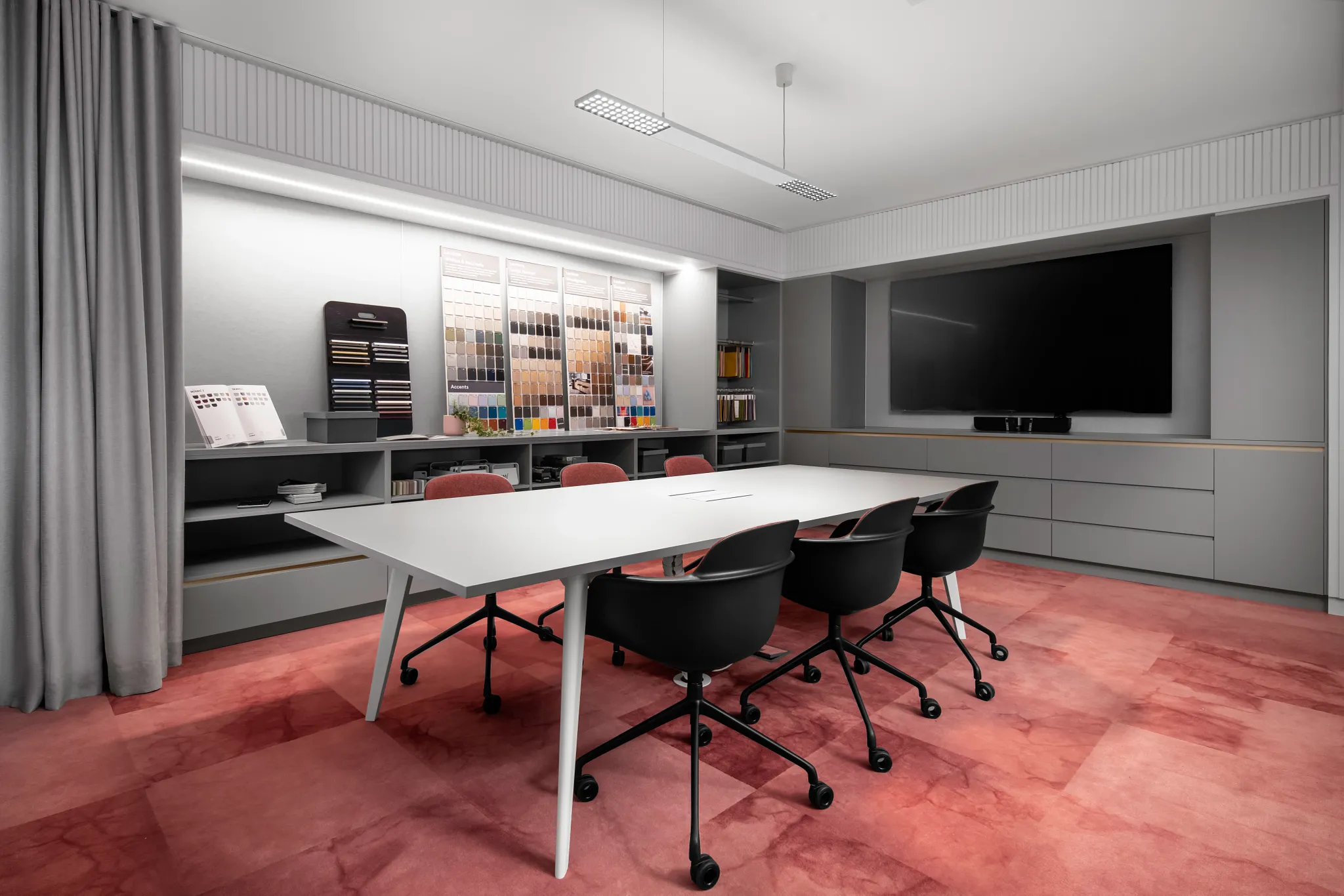 Modern showroom with a variety of colorful carpet swatches displayed on a wooden wall, featuring a mix of blue, green, orange, pink, and gray tones, with industrial lighting and shelving in the background