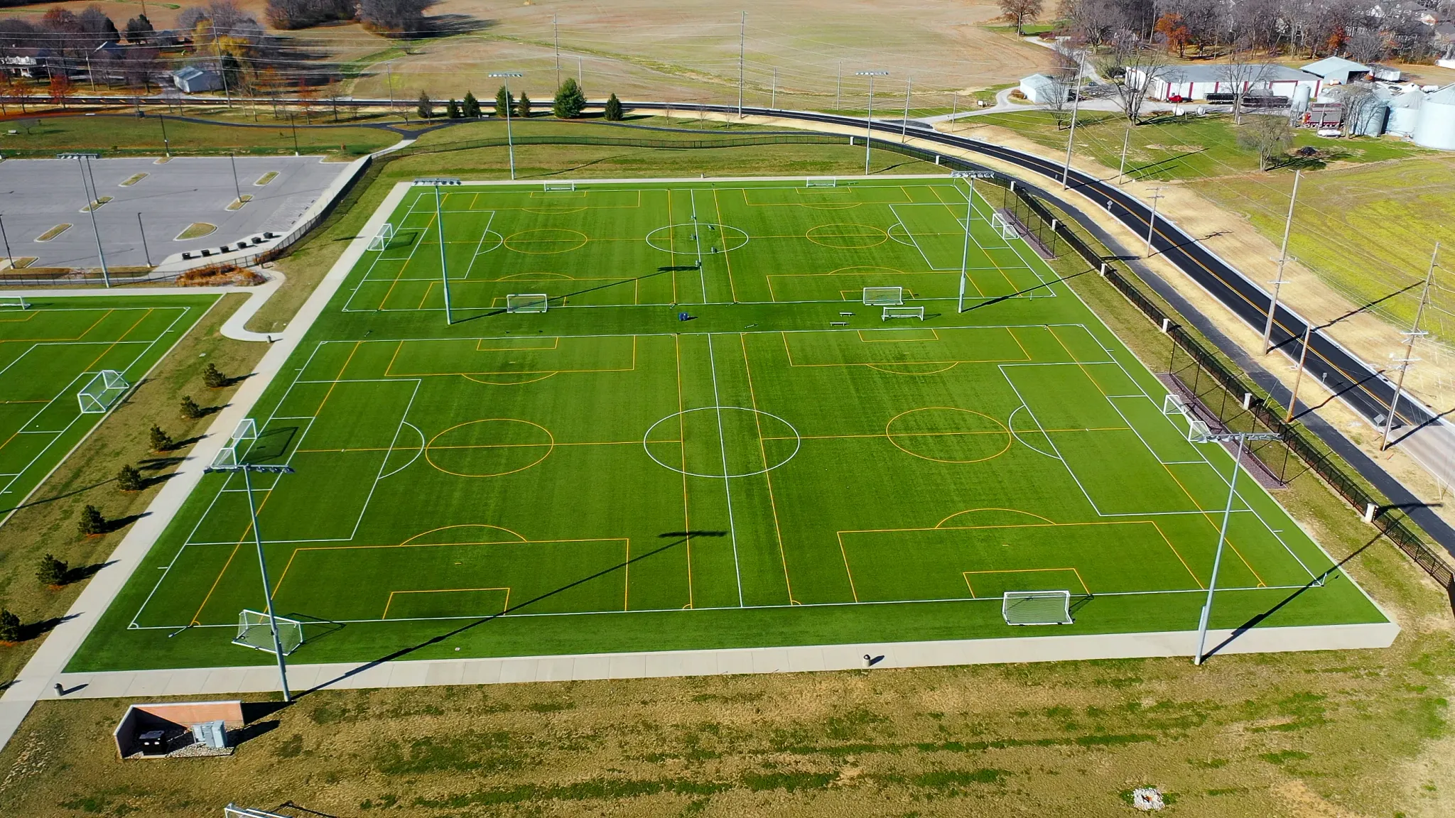 Aerial view of a large outdoor sports complex featuring multiple artificial turf soccer fields with white and orange field markings