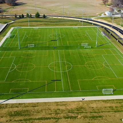 Outdoor sports complex with artificial turf soccer fields. Aerial view of a large outdoor sports complex featuring multiple artificial turf soccer fields with white and orange field markings