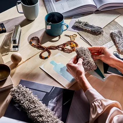 Explore Our Premium Carpet Swatches in Modern Gray and Beige Tones Woman examining various carpet swatches in shades of gray and beige on a wooden table